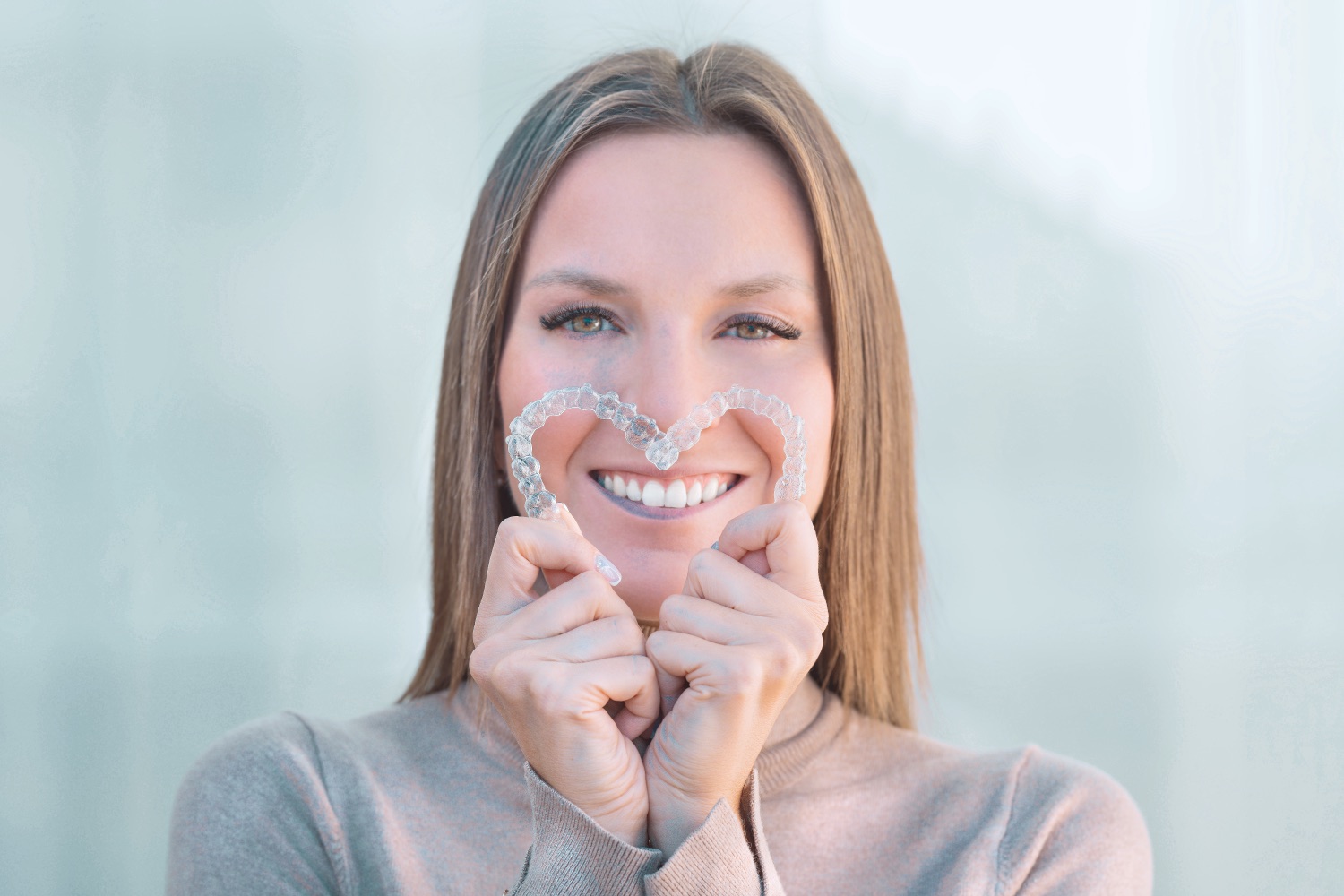 Smiling woman holding clear aligners in a heart shape